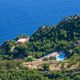 Veduta aerea di una località montuosa con vegetazione lussureggiante e vista sul mare blu.