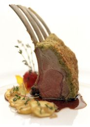 Lammkotelett mit Kräuterkruste, Garnitur und Sauce auf weißem Teller.