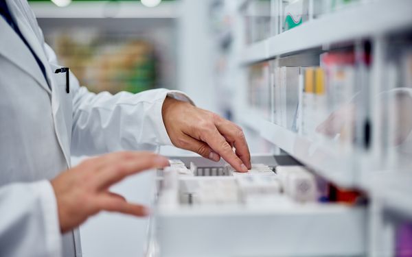 Ein Apotheker sucht in einem Apothekerschrank nach dem richtigen Medikament.