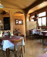 Gemütliches Restaurant mit Holzwänden, gedeckten Tischen und Blumen in einer sonnigen Atmosphäre.