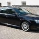 Schwarzes Auto, seitlich auf Pflastersteinen geparkt, vor einer weißen Wand.