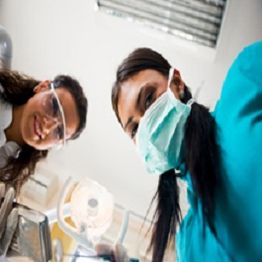 Two dental professionals, one in a mask, looking down, with overhead light visible above.