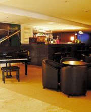 Sala de estar elegante com piano preto, cadeiras de couro, bar e imagem de homem na parede.