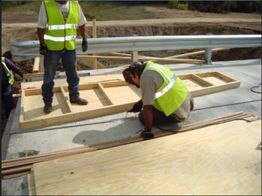 Workers in safety vests building a wooden structure on a bridge.