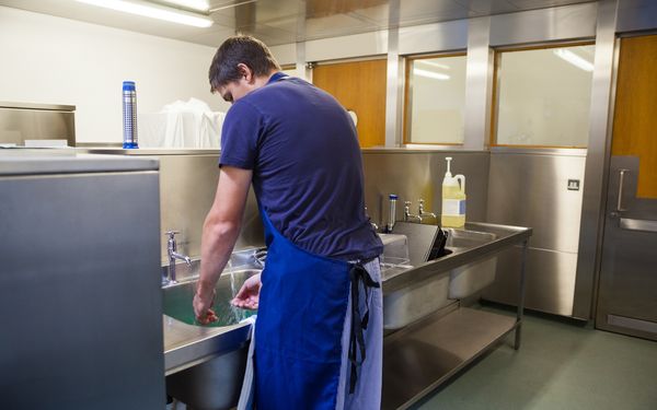 Ein junger Mann wäscht seine Hände an einem Waschbecken in einer Gastronomieküche.