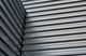 Close-up of metal corrugated siding at an angle, creating geometric patterns and shadows.