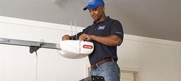 Technician installing a garage door opener while standing on a ladder.
