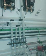 Tuberías de plástico y metal en una instalación industrial sobre una pared blanca.