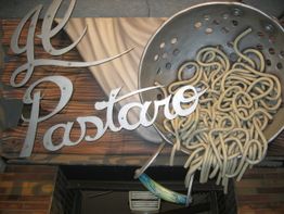 Metallschild mit Schriftzug "Il Pastaro" und Nudeldesign auf einem Holzuntergrund.