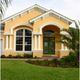 Yellow house with arched windows, green door, and manicured lawn under a cloudy sky.