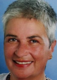 Ältere Frau mit grauen kurzen Haaren lächelt vor blauem Hintergrund.