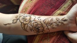 Blumentattoo auf einem Unterarm, filigran gestaltet auf einem bunten Stoffhintergrund.