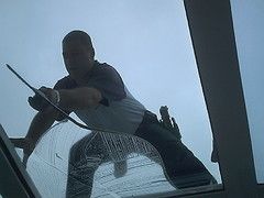 Ein Mann reinigt ein großes Fenster von außen mit einem Abzieher.