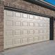 White garage door set in a brick wall, shown on a sunny day.
