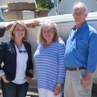 Three people standing and smiling in front of a boat outdoors.