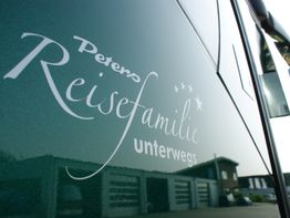 Text "Reisefamilie unterwegs" auf einem Fahrzeug, im Hintergrund ein Gebäude.