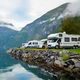 RVs parked beside a scenic lake, with mountains and clouds in the background.