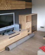 Modernes Wohnzimmer mit Holzmöbeln, Fernseher, Sofa und aufgerolltem Teppich auf dem Boden.