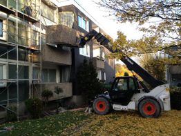 Teleskoplader entfernt Balkon von einem Gebäude. Gerüst und Herbstlaub im Hintergrund.