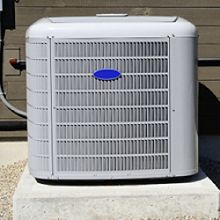 Outdoor air conditioning unit on a concrete slab in front of a wooden wall.