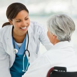 Doctor smiling at a patient in a wheelchair, offering support in a medical setting.