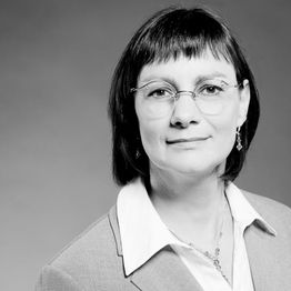 Eine Frau mit Brille in Anzug und offenem Haar blickt ernst in die Kamera, schwarz-weiß Aufnahme.