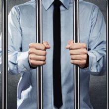Person in a dress shirt and tie gripping jail cell bars.