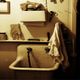 Old-fashioned sink with a towel, shelves, and various items on a beige wall.