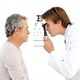 Doctor examining an older man's eyes with an eye chart in the background.