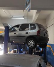 Carro prata elevado em plataforma de oficina mecânica, capô aberto, ambiente iluminado.