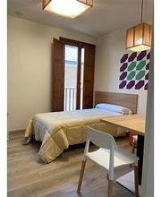 Habitación simple con cama, escritorio, silla y decoración de hojas en la pared.