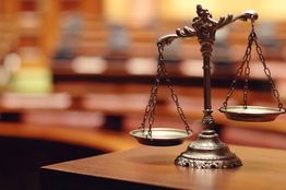 Bronze scales of justice on a desk, blurred courtroom in the background.