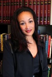A woman in a black outfit stands in front of bookshelves, smiling at the camera.
