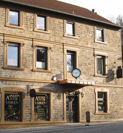Zweistöckiges Steingebäude mit Uhrengeschäft, großer Wanduhr und mehreren Fenstern.