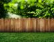 Wooden fence with a lush green lawn and leafy trees in the background.