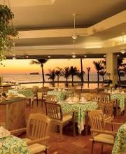 Restaurante elegante con vistas al mar al atardecer, mesas decoradas con manteles verdes.