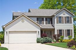 Two-story house with garage, surrounded by trees and shrubs, under a clear blue sky.
