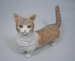 Kleine Katzenfigur mit rot-weißem Fell und großen Augen auf grauem Hintergrund.