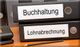 Ordner auf einem Tisch, beschriftet mit "Buchhaltung" und "Lohnabrechnung", daneben ein Bleistift.