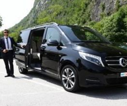 Eine Person im Anzug steht neben einem schwarzen Mercedes-Van im Freien.