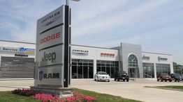 Car dealership exterior with Chrysler, Dodge, Jeep, and RAM signs under a clear sky.