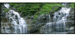 Wasserfall fließt über Felsen mit üppigem Grün im Hintergrund.