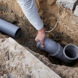 Person aligning PVC pipes in a trench.