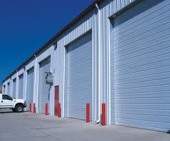Row of industrial garage doors against a clear blue sky, with a parked white truck nearby.
