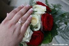 Hand mit Ring über Strauß aus roten und weißen Rosen.