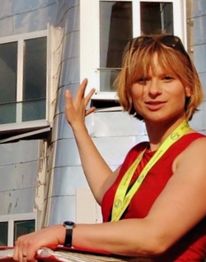 Frau in rotem Top steht vor modernem Gebäude mit silberner Fassade und Fenstern.