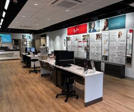 Interieur van een brillenwinkel met houten vloer, tafels en bril displays aan de muren.