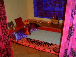 Letto con cuscini colorati, incorniciato da tende e luci soffuse in una stanza accogliente.