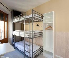 Schlafzimmer mit Etagenbett, offenem Kleiderschrank, Tisch und hellem Fenster.