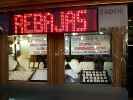 Escaparate de joyería con letrero luminoso de "REBAJAS" y carteles de compra de oro.